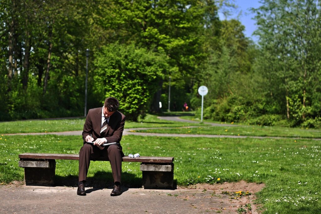 公園のベンチで勉強するスーツの男性